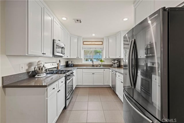 kitchen featuring light tile patterned floors, a sink, stainless steel appliances, white cabinets, and dark countertops