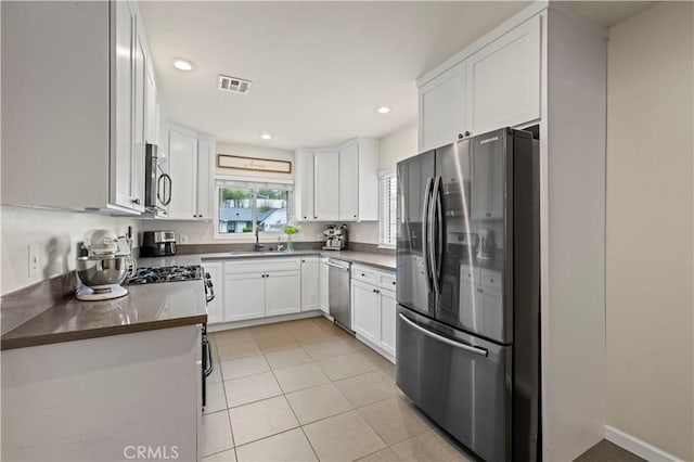 kitchen with visible vents, a sink, white cabinetry, stainless steel appliances, and light tile patterned flooring