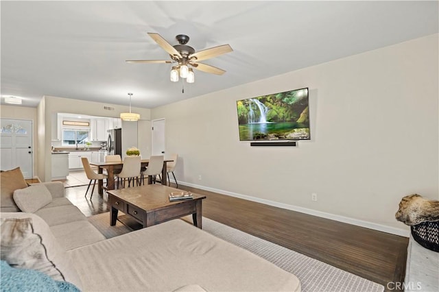 living room featuring light wood-type flooring, baseboards, and ceiling fan