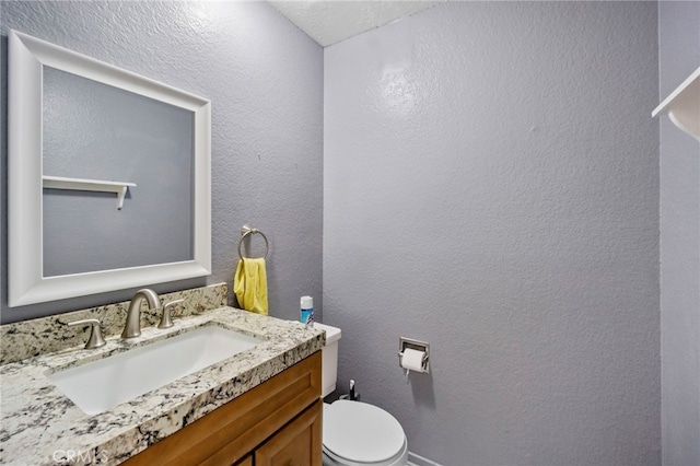 half bathroom featuring toilet, vanity, and a textured wall