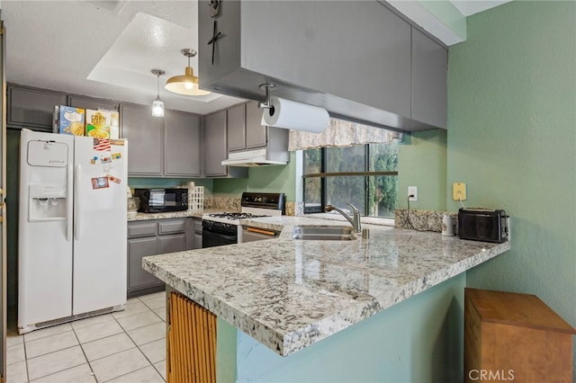 kitchen with a tray ceiling, white refrigerator with ice dispenser, black microwave, under cabinet range hood, and gas range