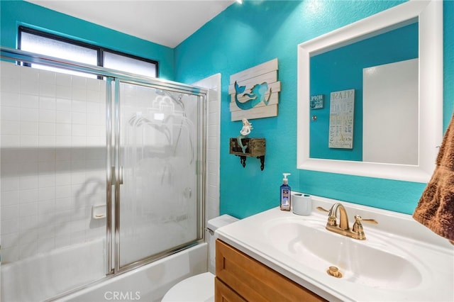 bathroom featuring combined bath / shower with glass door, toilet, vanity, and a textured wall