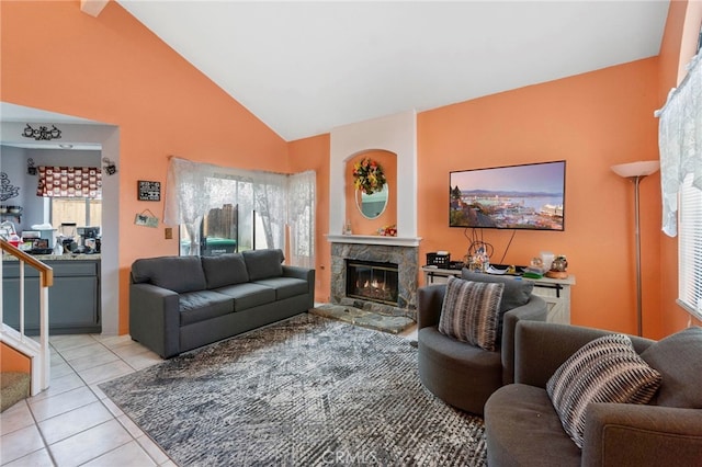 living room featuring a stone fireplace, light tile patterned floors, and high vaulted ceiling