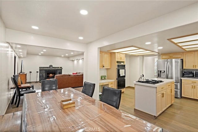 dining area featuring light wood-type flooring, a warm lit fireplace, and recessed lighting