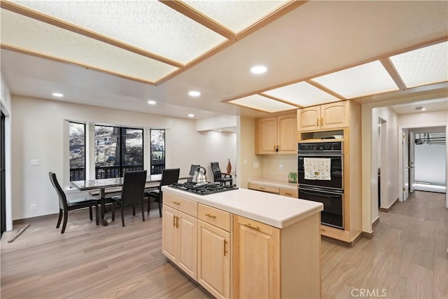 kitchen featuring a center island, light countertops, light brown cabinetry, light wood-type flooring, and black appliances