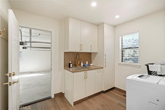 clothes washing area featuring cabinet space, washer and dryer, light wood-style floors, a sink, and recessed lighting