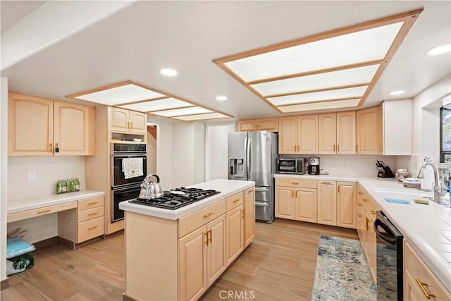 kitchen featuring light wood finished floors, a sink, black appliances, light brown cabinets, and built in desk