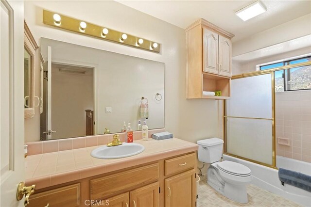 full bathroom featuring combined bath / shower with glass door, vanity, and toilet