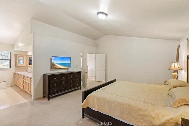 bedroom featuring vaulted ceiling, ensuite bathroom, a sink, and light colored carpet