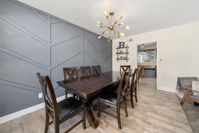 dining area with light wood finished floors, visible vents, a textured ceiling, a chandelier, and a decorative wall