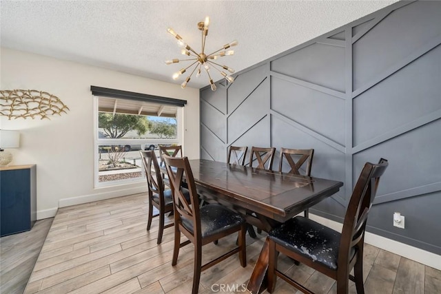 dining area with a decorative wall, an inviting chandelier, a textured ceiling, wood finished floors, and baseboards