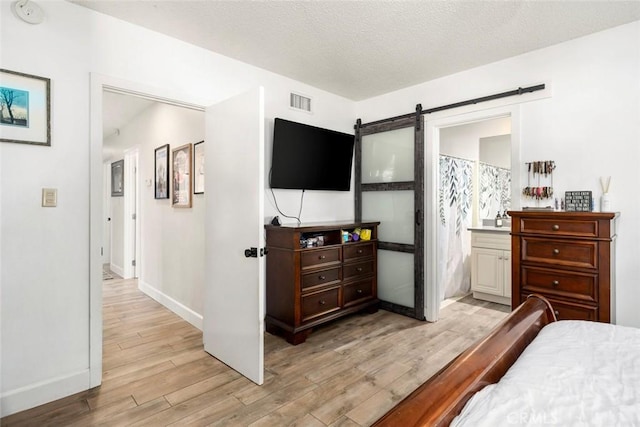 bedroom with visible vents, light wood-style flooring, a barn door, a textured ceiling, and baseboards