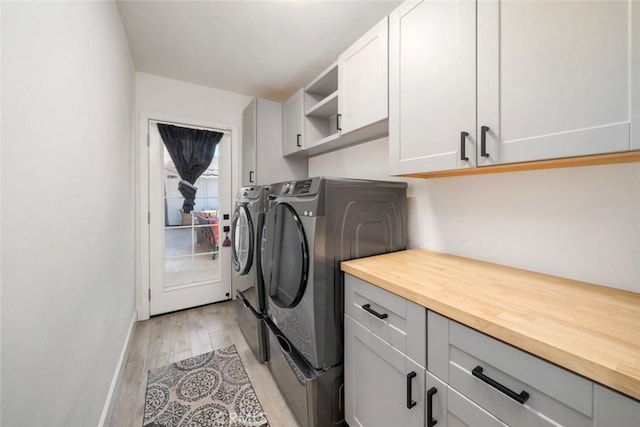clothes washing area with cabinet space, baseboards, washer and clothes dryer, and light wood finished floors