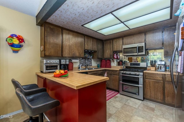 kitchen featuring stainless steel appliances, butcher block countertops, a peninsula, a sink, and a kitchen bar