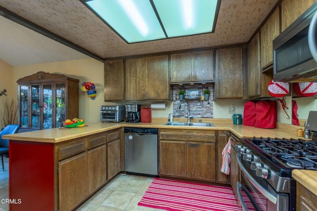 kitchen featuring wood counters, a peninsula, stainless steel appliances, a textured ceiling, and a sink