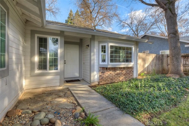 doorway to property with brick siding and fence