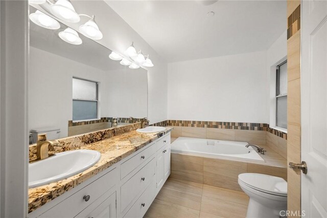 full bathroom featuring toilet, a garden tub, double vanity, and a sink