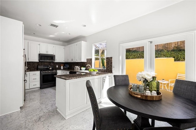 kitchen with visible vents, stainless steel microwave, a peninsula, gas range oven, and backsplash