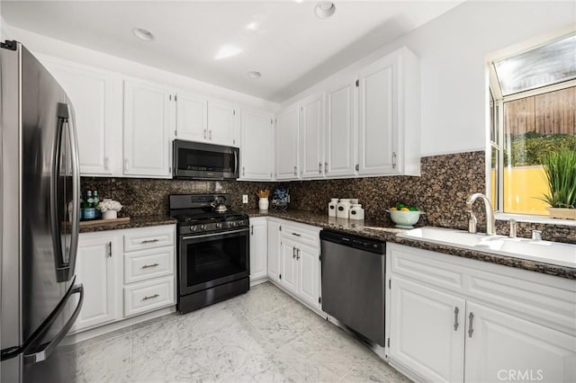 kitchen with dark stone counters, appliances with stainless steel finishes, a sink, and white cabinets