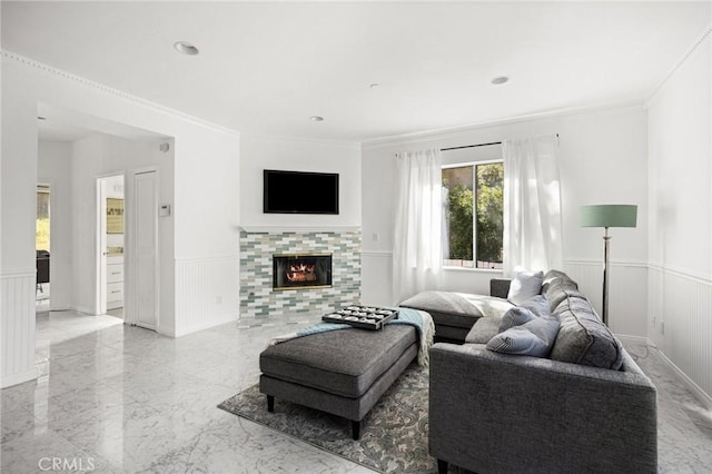 living area featuring marble finish floor, crown molding, a decorative wall, a tiled fireplace, and wainscoting