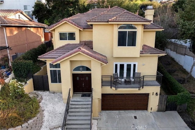 mediterranean / spanish home with stucco siding, concrete driveway, fence, a garage, and a tiled roof