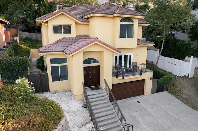 mediterranean / spanish-style home with an attached garage, fence, a tiled roof, concrete driveway, and stucco siding