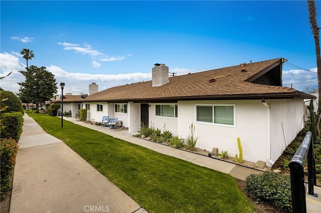 rear view of property featuring a patio, roof with shingles, a lawn, stucco siding, and a chimney