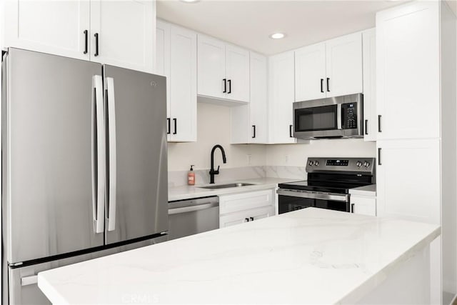 kitchen featuring stainless steel appliances, a sink, light stone countertops, and white cabinets