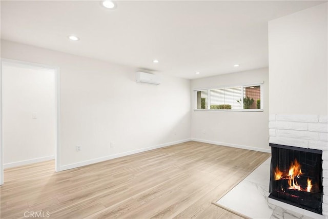 unfurnished living room featuring a wall mounted AC, baseboards, light wood-type flooring, a brick fireplace, and recessed lighting