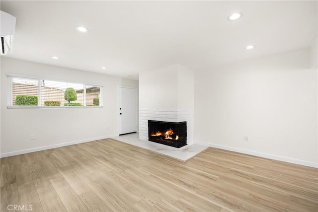 unfurnished living room featuring light wood-type flooring, a brick fireplace, baseboards, and recessed lighting