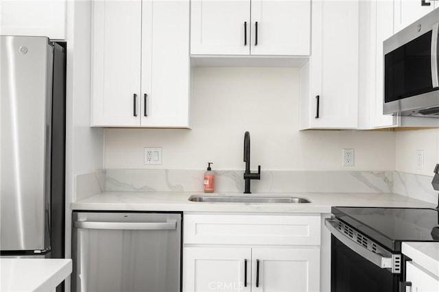 kitchen with light stone counters, white cabinetry, stainless steel appliances, and a sink