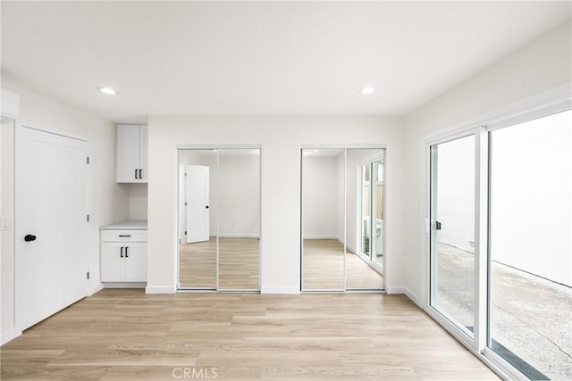 unfurnished bedroom featuring multiple closets, light wood-type flooring, baseboards, and recessed lighting