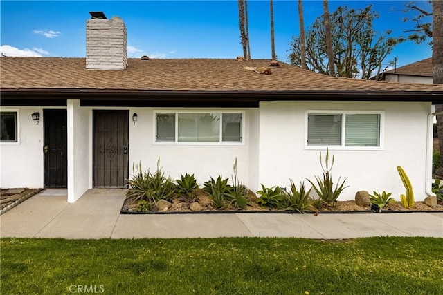 ranch-style home featuring roof with shingles, a chimney, and stucco siding