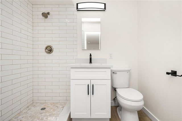 full bath featuring toilet, baseboards, tiled shower, and vanity