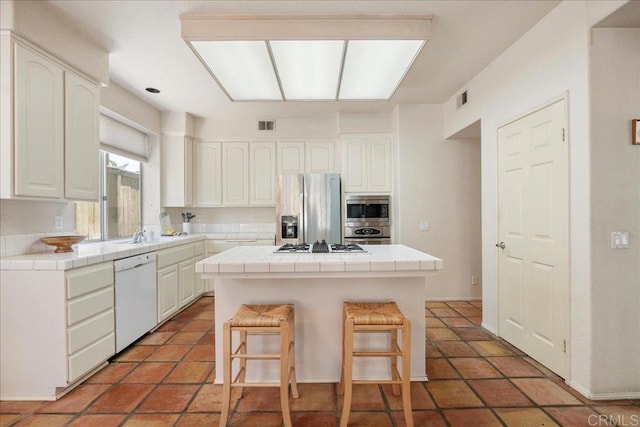 kitchen featuring appliances with stainless steel finishes, a center island, tile counters, and white cabinetry