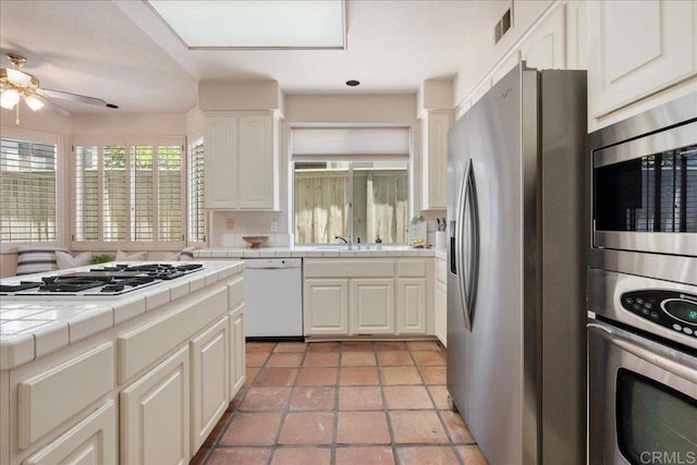 kitchen with stainless steel appliances, tile counters, visible vents, white cabinetry, and a sink