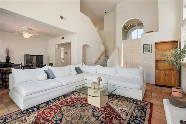 living area featuring light tile patterned floors, visible vents, a high ceiling, a ceiling fan, and stairs