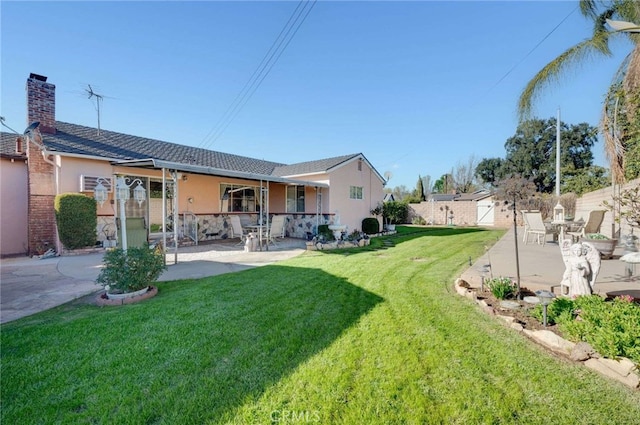 back of house with fence, stucco siding, a chimney, a yard, and a patio area