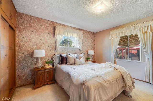 bedroom featuring wallpapered walls, light colored carpet, and a textured ceiling