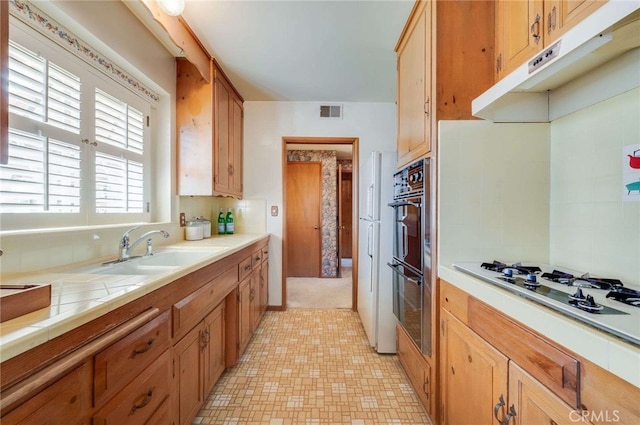 kitchen featuring visible vents, a sink, tile countertops, double oven, and white gas cooktop