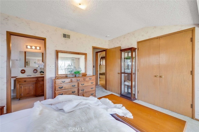 bedroom with wallpapered walls, vaulted ceiling, visible vents, and a textured ceiling