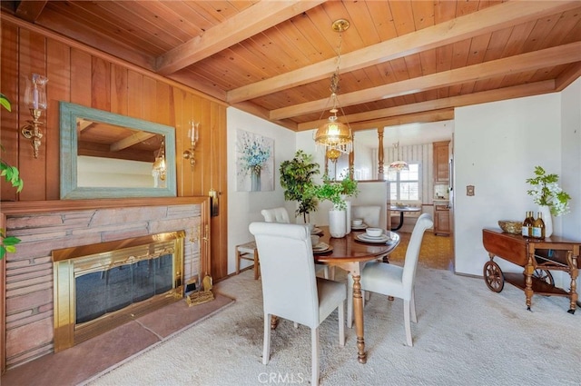 dining area featuring beam ceiling, a stone fireplace, wood ceiling, and carpet