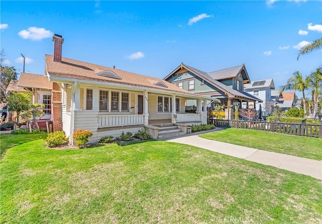 view of front of property featuring covered porch, a front lawn, a chimney, and fence