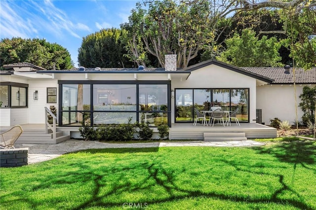 back of property with a sunroom, a chimney, a deck, a yard, and stucco siding