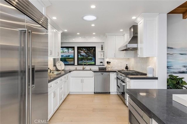 kitchen featuring white cabinets, a sink, wall chimney range hood, and built in appliances