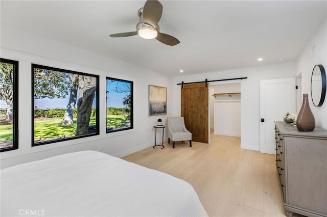 bedroom featuring a barn door, baseboards, ceiling fan, a spacious closet, and light wood-style floors