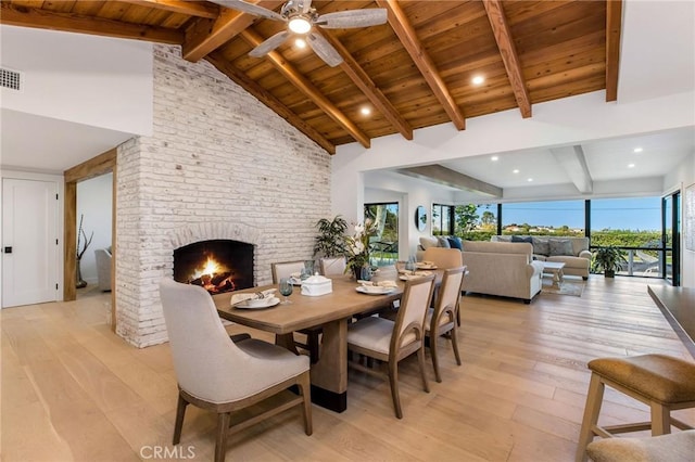 dining room with light wood-style floors, a brick fireplace, wooden ceiling, and beam ceiling