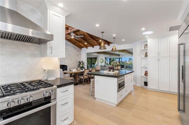 kitchen with lofted ceiling with beams, wall chimney range hood, dark countertops, and stainless steel appliances