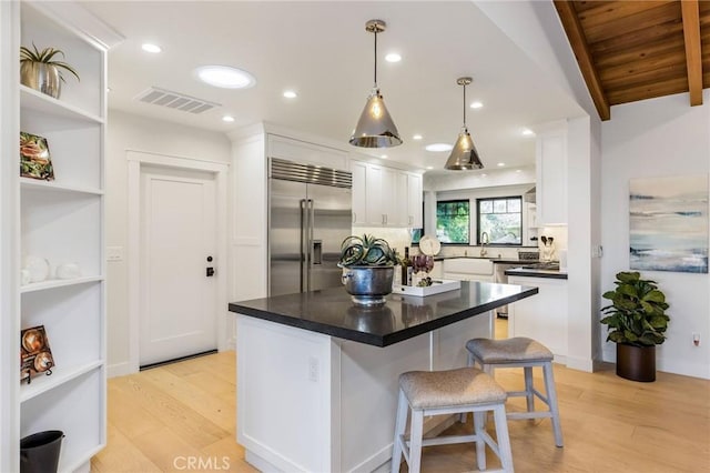 kitchen featuring visible vents, white cabinets, dark countertops, light wood-style flooring, and built in fridge