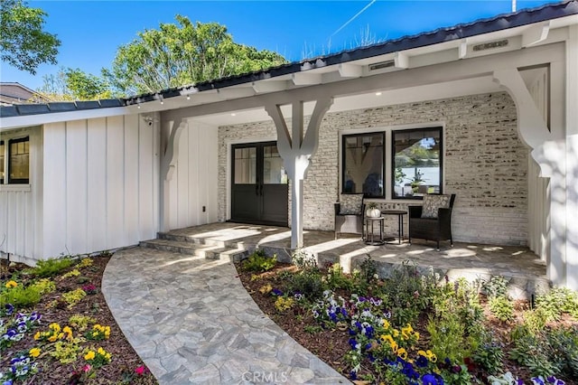 view of exterior entry with covered porch, board and batten siding, and brick siding